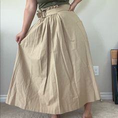 A Classic Belted Skirt With A Fun Asymmetrical Twist. It Has A Roomy Pocket On One Side, And A Gathered Elastic Waistband That Allows It To Fit A Range Of Sizes Summer Asymmetrical Belted Skirt, High Waist Khaki Skirt For Spring, Chic High Waist Khaki Skirt, Beige Pleated Asymmetrical Skirt, Beige Asymmetrical Flowy Maxi Skirt, Beige Asymmetrical Relaxed Skirt, Beige Flowy Asymmetrical Maxi Skirt, Flowy Asymmetrical Beige Maxi Skirt, Asymmetrical Gathered Skirt For Day Out