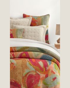 a bed with colorful comforters and pillows on it's headboard, next to a night stand