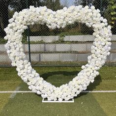 a heart shaped wreath made out of white flowers on top of a green soccer field