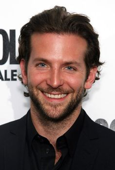 a man with a beard smiling at the camera while wearing a black shirt and blazer