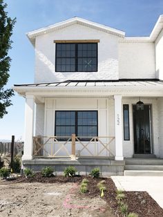 a white two story house with black windows and wooden railings on the front porch