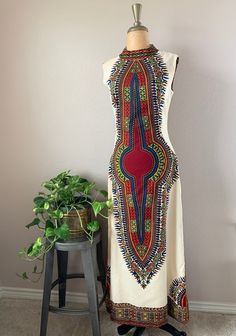 1970s sleeveless bohemian maxi dress. Dashiki style print, floor length and high neck collar. Back plastic zipper with hook and eye closure above zipper. Print is red, blue, green, yellow, orange. Fabric is off white. Beautifully tailored with bust darting and tapering at waist. Dress has some lining.  Tag: None  SIZE  Modern size: S Bust: 36" Waist: 29" Hip: 38" Length: 55" Measurements are taken with the garment lying flat, and un-stretched. Bust, waist and hip measurements are doubled. Sleeve Printed Floor-length Maxi Dress For Festivals, White Sleeveless Boho Print Maxi Dress, Hippie Multicolor Long Maxi Dress, Vintage White Sleeveless Maxi Dress, Bohemian Maxi Dress With Vintage Print, Multicolor Vintage Maxi Dress With Boho Print, Fitted Boho Print Maxi Dress, Multicolor Boho Print Floor-length Maxi Dress, Fitted Sleeveless Hippie Dress