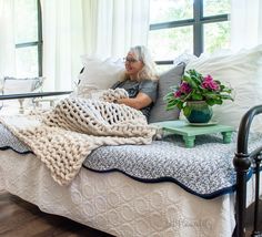 a woman sitting on top of a bed next to a window with flowers in it