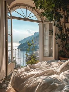 an open window with a view of the water and mountains outside it, in front of a bed