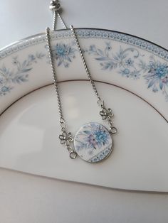 a white plate with blue flowers on it and a silver chain hanging from the edge