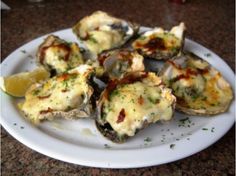 a white plate topped with oysters covered in sauce and garnished with lemon wedges