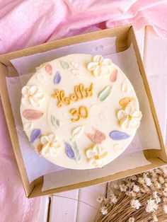 a cake in a box with the word hello written on it and some dried flowers