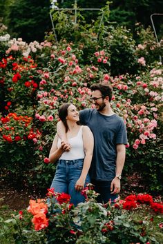 a man and woman are standing in front of some red flowers with their arms around each other