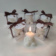 four small candles in clear boxes with brown ribbon around them on a white tablecloth