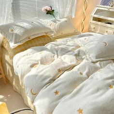 a bed with white sheets and gold stars on it, next to a window in a bedroom