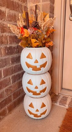 three pumpkins stacked on top of each other in front of a brick wall and door