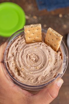 a hand holding a glass with some food in it and crackers on the side