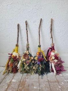 four brooms are lined up on the floor and one is decorated with flowers, feathers and twigs