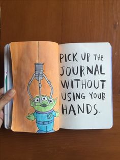 a hand holding an open book with writing on it and a drawing of a cartoon character hanging from a hook