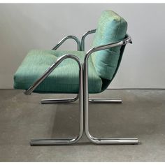 a green chair sitting on top of a cement floor next to a white wall with a metal frame