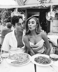 a man and woman sitting next to each other at a table with plates of food