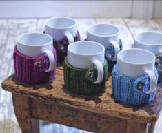 six coffee mugs sitting on top of a wooden table covered in knitted sweaters