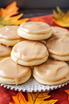 a plate full of cookies with frosting on it and fall leaves in the background