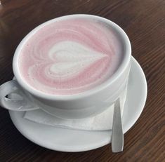 a white cup with pink liquid in it on a saucer next to a spoon