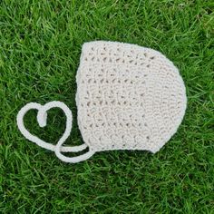 a crocheted hat laying on top of green grass with a white string attached to it