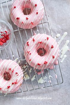 three donuts with pink frosting and sprinkles on a cooling rack