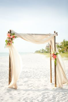 an outdoor wedding setup on the beach with white draping and flowers at the top