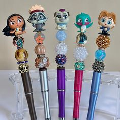 five different colored pens are lined up in a clear holder with beaded charms on them