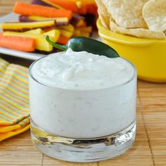 a small glass bowl filled with white sauce next to tortilla chips and vegetables