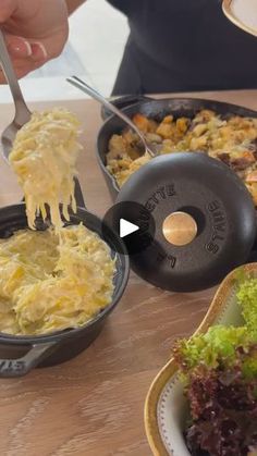 a person is eating food out of a pan on a table with other dishes and utensils