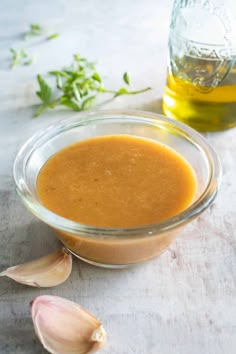 a glass bowl filled with sauce next to an open bottle of oil and garlic florets