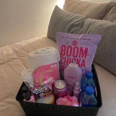 a black basket filled with lots of items on top of a bed next to pillows