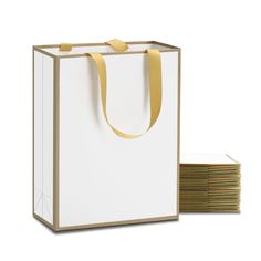 a white paper bag with gold handles next to stacks of papers on a white background