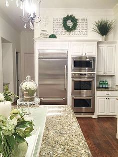 a kitchen with white cabinets and granite counter tops, stainless steel appliances and flowers in vases