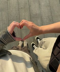 two people sitting on the ground making a heart shape with their hands while holding each other's fingers