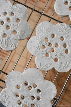 some white buttons are sitting on a wire rack with holes in the middle that have been cut out to look like flowers