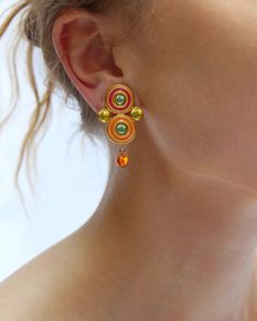 These vintage enamel earrings are pure whimsical fun. They feature two enamel spirals set with green glass stones, flanked on either side by a contrasting citrine-colored stone. I love the orange drops that dangle beneath, adding graceful movement. The are finished with a clip-on lever back; vintage clip-ons are so much more comfortable and secure to wear compared to their modern counterparts, largely due to the quality and thought that went into their hand-made construction. They measure 42 mm long x 22 mm at widest point. Great vintage condition. With any questions about the specific condition or size, please send me a message for additional photos or measurements, or email shop@verybreezy.com Visit my site more vintage fashion: verybreezy.com  @VERYBREEZY -- Follow along on Instagram fo Orange Enamel Dangle Jewelry, Orange Clip-on Earrings As Gift, Orange Clip-on Earrings For Gift, Orange Clip-on Jewelry For Gift, Vibrant Orange Dangle Jewelry, Unique Orange Metal Earrings, Vintage Clip, Enamel Earrings, Style Expert