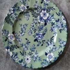 a green plate with blue and white flowers on it sitting on a gray tablecloth