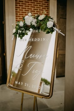 a sign with flowers on it sitting in front of a brick building next to a door