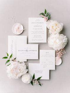 the wedding stationery is laid out on top of each other with white flowers and greenery