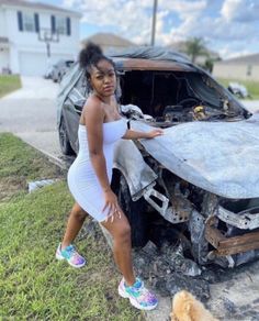 a woman standing in front of a car that has been destroyed and is next to a dog