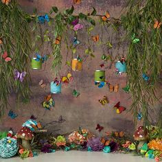 a bunch of paper butterflies hanging from the ceiling above some plants and flowers in front of a wall