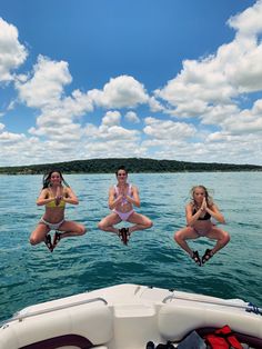 three women in bikinis are jumping off the back of a boat