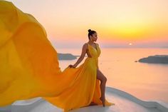 a woman in a yellow dress standing on the edge of a cliff