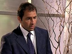 a man wearing a suit and tie standing in front of a wall with branches on it