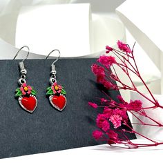 These Dainty Heart Earrings are the ultimate must-have. Expertly handcrafted and exquisitely hand-painted with a bold red enamel finish, playful pink flowers, and vibrant green leaves. Perfect for ladies and girls alike, these adorable dangling heart earrings are an ode to Frida's unique style. A perfect gift for any Fridalover, these Mexican-inspired accents are sure to put a smile on their face. Looking for a charming, one-of-a-kind present that won't break the bank? Look no further than these delightful hand-painted heart earrings inspired by Frida! Each earring is carefully crafted and meticulously painted by hand in our studio, and it takes a considerable amount of time and extreme attention to detail to finish them and finally offer them for sale. “It is always the simple that produc Red Flower Charm Jewelry For Valentine's Day, Heart Charm Enamel Earrings, Heart-shaped Enamel Earrings With Charm, Valentine's Day Heart Charm Enamel Earrings, Red Dangle Flower Earrings For Valentine's Day, Pink Hand Painted Heart Jewelry, Cute Red Hand-painted Jewelry, Cute Red Hand Painted Jewelry, Cute Hand Painted Red Jewelry