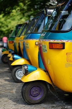 row of yellow and blue cars parked on the side of the road with trees in the background