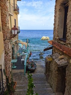 an alley way leading to the ocean with stairs going up and down in between two buildings