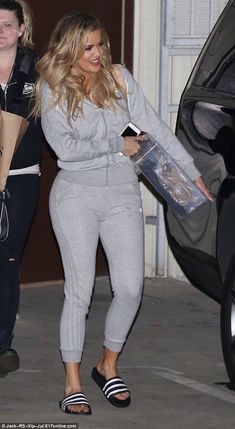 a woman in grey sweatsuit walking next to a black car and another woman with her handbag