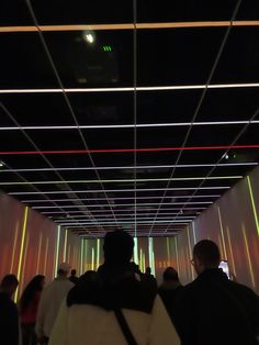 people are walking through a tunnel with neon lights on the ceiling and walls behind them