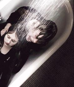 two people sitting in a bathtub with water pouring from the faucet over their heads